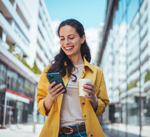 Woman walking on the sidewalk at urban setting and looking at her phone